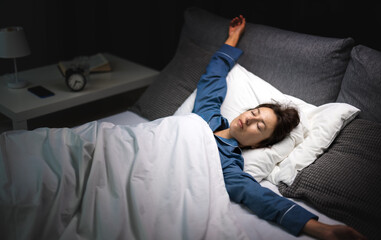 Fototapeta premium Beautiful middle aged woman lying in bed with closed eyes while sleeping well at night. Relaxed dark haired lady in pajamas enjoying sweet dreams at home.