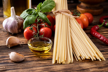 raw Pasta spaghetti with tomatoes, garlic olive oil basil on rustic wooden background