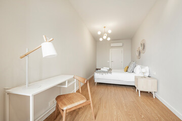 Fototapeta na wymiar Simple white desk with lamp and wooden chair in a vacation rental apartment bedroom