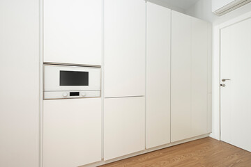 Wall covered with white kitchen cabinets and a matching microwave in a vacation rental apartment
