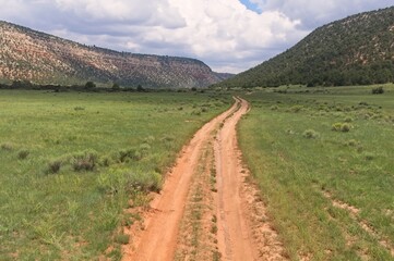 Naklejka premium A dirt road runs through a New Mexico valley flanked by scrub covered mountains.