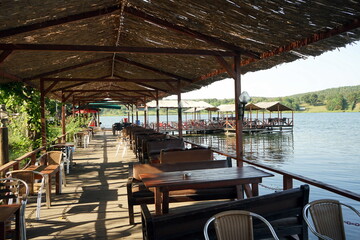 Tische und Bänke auf Schiffsdielen mit offenen Pavillons im Sommer bei Sonnenschein am Ufer des...