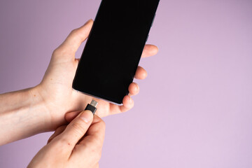 Mobile smart phones charging. Woman hands plugging a charger in a smartphone on purple background