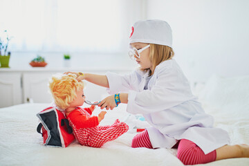 Adorable toddler girl in white coat playing doctor