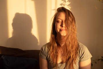 Young woman close eyes and relaxation in warm rays of sunset. Warm calm portrait of girl indoor