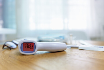 Close-up infrared forehead thermometer gun after check body temperature for virus covid-19 symptoms in body with rapid antigen test kit on desk in blur background.