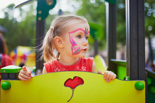 Little preschooler girl with butterfly face painting outdoors