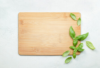 wooden cutting board and fresh basil leaves on light gray concrete background