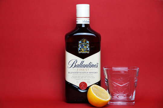 ballantine's whiskey bottle, glass and lemon on red background copy space