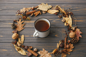 Hello autumn. Cup of tea in autumn wreath. Autumn leaves, berries, nuts, anise, acorns in circle with mug of hot tea on rustic dark wood.  Happy Thanksgiving