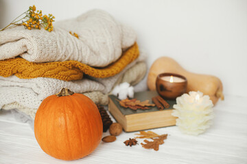Fototapeta na wymiar Pumpkin, cozy sweaters, autumn leaves, burning candle and vintage book on white wooden background in room. Hello autumn, cozy slow living. Happy Thanksgiving and Happy Halloween