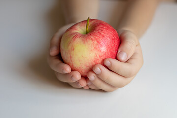Ripe juicy beautiful red apple in the hands of a child. Light background, closeup.