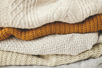 Cozy knitted sweater background. Pile of white, yellow and beige knit sweaters close up. Hello autumn. Stylish wardrobe for cold season