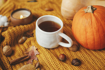 Obraz na płótnie Canvas Warm cup of tea on yellow knitted sweater with pumpkins, autumn leaves, burning candle. Cozy autumn slow living. Happy Thanksgiving and Halloween. Hello fall season