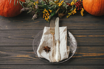 Modern plate with vintage cutlery, linen napkin, anise on wooden table with pumpkins and autumn...