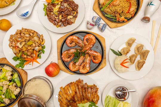 Top view image of popular Chinese restaurant dishes. Grilled prawns, steamed gyozas, Peking duck, chicken with almonds, veal with vegetables, sautéed noodles.