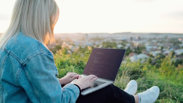 Smart Female IT Programer works on a hill on the background of the city, sunset. High quality 4k footage