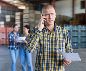 Man talking on phone and holding document in hand. Two women standing behind and discussing.