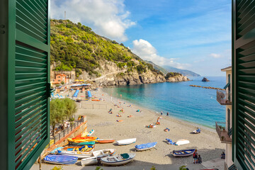 Window view of the sandy beach and clear blue water on the old side of the village of Monterosso Al Mare on the Ligurian coast of Cinque Terre, Italy.