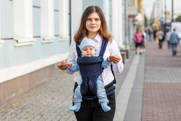 Mother with little child in sling walks on street.