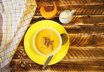 Pumpkin soup in a yellow plate on a wooden background.