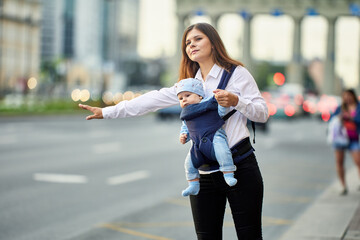 Mother with child in sling is stopping taxi on street.