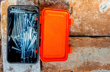picture of a box of concrete nails, on a red brick background.