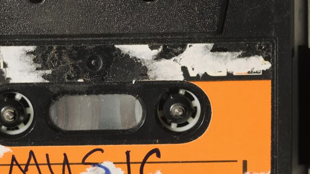 Music - inscription on cassette in old tape recorder. old red cassette with torn label being played on broken sound player, close up view, dolly motion.