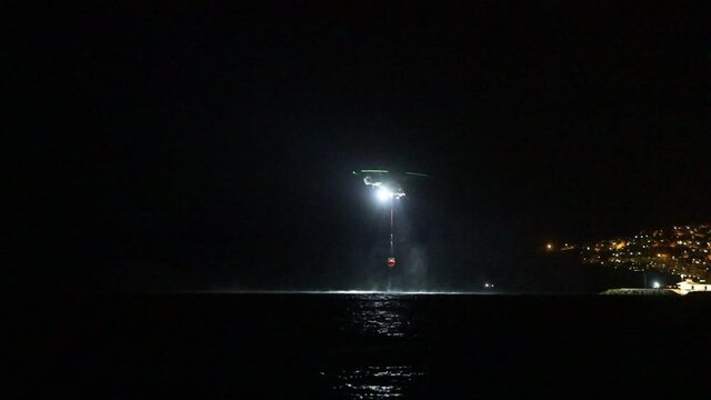 night vision firefighting helicopter takes water from the sea.