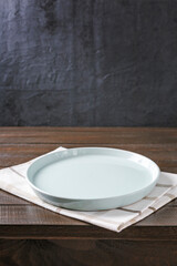Empty plate on napkin on wooden table over grunge blue background.