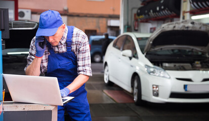 Auto mechanic with laptop talking on mobile phone in auto repair shop