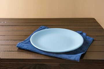 Empty plate on napkin on wooden table over grunge blue background.