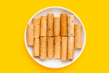Thai crispy coconut rolls in white plate on yellow background.