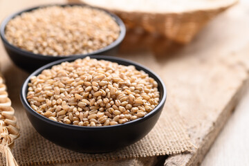 Wheat grain in a black bowl on wooden background
