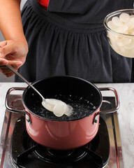 Indonesian Female Hand Put Sugar Palm Fruit (Kolang Kaling or Cangkaleng) on a Boiling Water in a Pan at Indonesian Kitchen. Proces Making Manisan Kolang Kaling