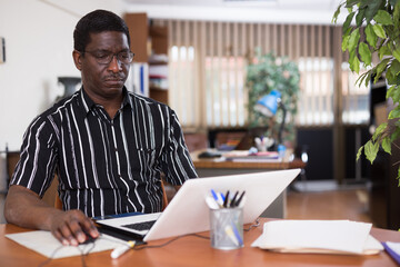 Obraz premium Focused african american man working for a large company types documentation on a computer while sitting at workplace ..in the office