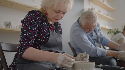 Three elderly people work on a potter's wheel in slow motion
