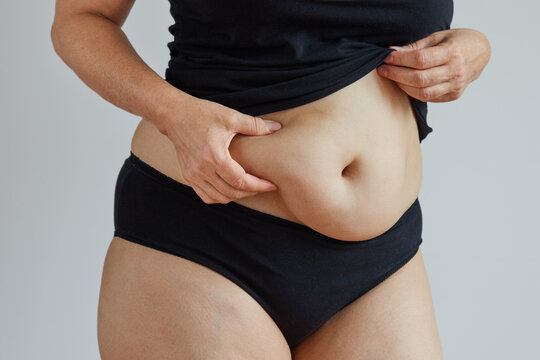 figure of a woman in black underwear pinches the fat on her belly with her hand