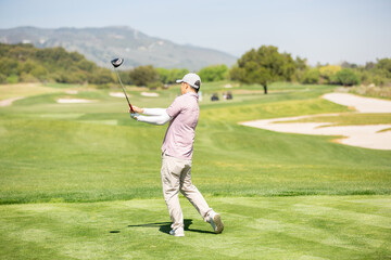 A view of a male golfer practicing his club swing on a golf course.