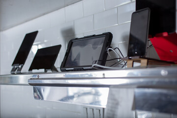 A view of several tablets used for food app deliveries, seen on a shelf in a restaurant kitchen.