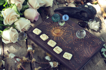Still life with magic witch book, runes, crystal and roses on wooden table.