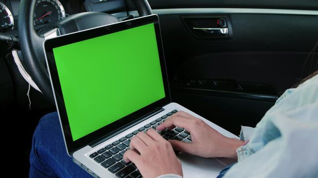 Asian woman sitting in a car typing on keyboard and using laptop computer with chroma key green screen display, social distancing during delta covid pandemic , freelance job, new normal concept