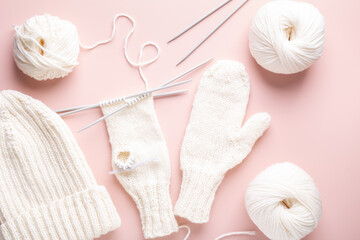 White wool knitting needles and knitted hat on pastel pink background. Female hobby knitting. Top view