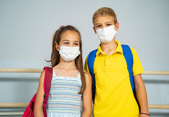 Two kids with  face masks and school bags next to gray wall. Back to school, coronavirus 