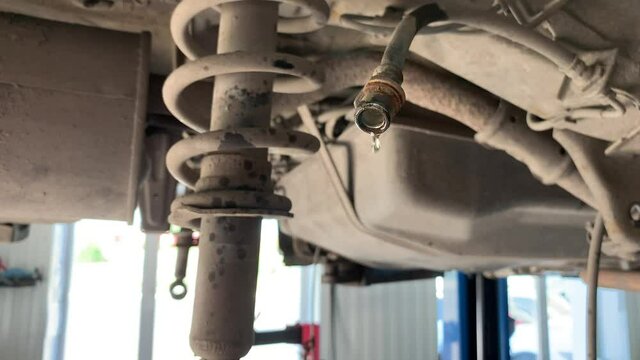 The car is in a car service station for the repair of the brake system. Brake fluid drips from the hose. The car is suspended on a lift in a car service station.