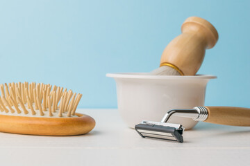 Fototapeta na wymiar A brush in a white bowl, a razor and a comb on a white table on a blue background.