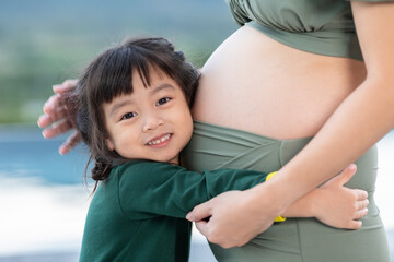 Adorable kid girl hugging pregnant mother belly to hearing sound of baby.Lovely little girl loving and waiting for newborn sister in her mother belly.Happy kid smile with tummy of her mom pregnancy