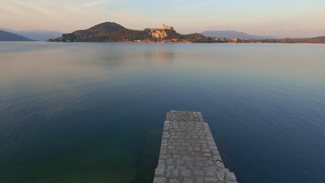 Peaceful establishing shot of concrete jetty on lake Maggiore calm water in Italy, Angera castle in background. Slow-motion