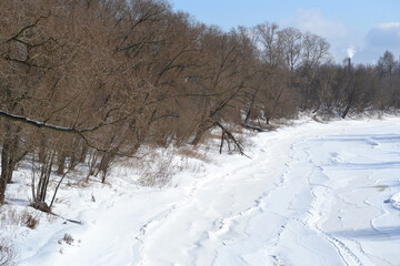 Walking paths on the snow-covered ice of the frozen river bed. Urban winter landscape on a sunny cold day in early spring on the river in March