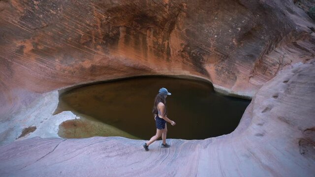 Young Female Hiker Walking on Sandstone Cliff Above Rainwater Pond in Wilderness of Utah, St. George Hiking Trail, Full Frame